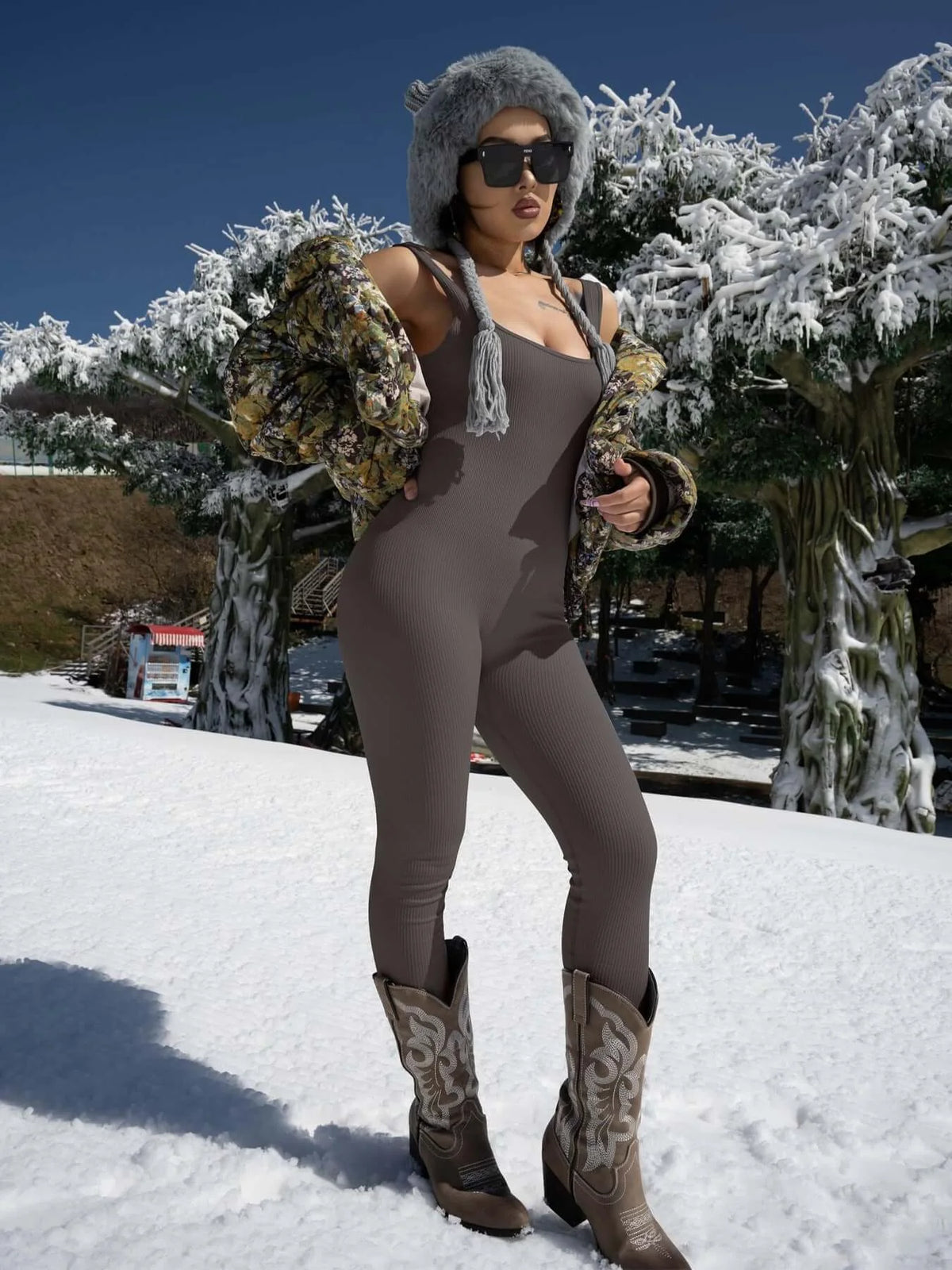 Woman in a stylish women’s jumpsuit with a winter jacket and boots in snowy outdoor setting, showcasing elegant and versatile fashion.